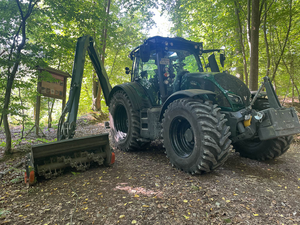 Schlepper mit Forstmulcher am Ausleger auf einem Waldweg
